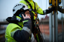 Male Rope Access Worker Talking On Phone Outside Window Of Building