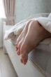 Feet under a light blanket on the bed, soft focus background