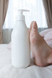White bottle with a cosmetic product on the background of feet under a light blanket on the bed