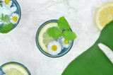 Fototapeta Kwiaty - Three drinks decorated with lemon, mint and flowers and big exotic leaf . Top view.