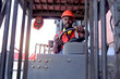 © Stella - Industrial worker man wearing safety bright neon red vest and helmet driving forklift car at plant factory industry, African American engineer male working at logistic shipping cargo container yard.