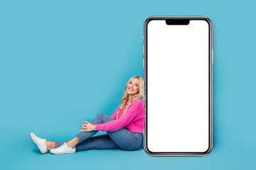 Canvas Print - Full body length size of sitting relaxed blonde hair woman near smartphone display new web constructor isolated on blue color background