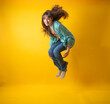 Energetic Young Woman Jumping with Joy on Yellow Background