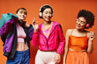 A group of beautiful women of different ethnicities standing together against an orange studio background.