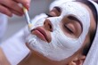Woman receiving a facial mask treatment at a spa with a brush application.