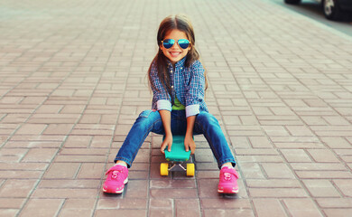 Stylish little girl child posing with skateboard on city street