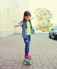 Wall Mural - Stylish little girl child posing with skateboard on city street