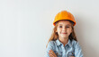 A young girl wearing a hard hat and a blue shirt. She is smiling and looking at the camera. outhful builder: Smiling child near a white wall, exploring career possibilities