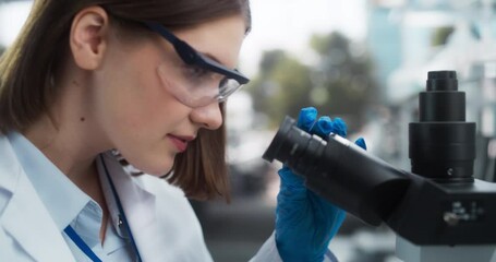 Poster - Close Up Portrait of a Female Microbiologist Wearing Safety Glasses and Looking Through the Microscope, Analyzing Sample Cells. Skillful Scientist Working in a Medical Science Laboratory