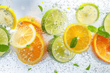 Fototapeta Tęcza - Carbonated drink, mint leaves and fruit slices of lemon, lime and orange floating in it. Summertime background.