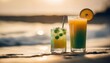 Two drinks on a beach, one is greenish yellowish drink with a straw in it