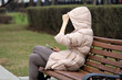 Girl in jacket with hood sitting with smartphone on а street bench in spring