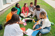 © Jose Calsina - Multiracial students using a laptop computert sitting in a circle on the grass, doing homework outside at university campus. Young high school people working together on a academy task or schoolwork