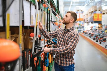 Wall Mural - a young man in a gardening equipment store chooses an electric trimmer for mowing lawn grass