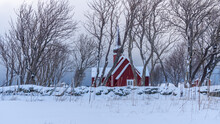 Rote Kirche In Flakstad Ist Schneebedeckt, Kahle Bäume Im Vordergrund
