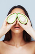 Beautiful girl with long dark hair covers her eyes with avocado halves. Diet, fruit, vegetarian food. Skin and body care