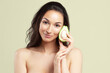 Young beautiful woman holding avocado half on pistachio background