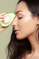 Wall Mural - Young white woman with long dark hair showing cut avocado. Fruit, unsaturated fats, diet