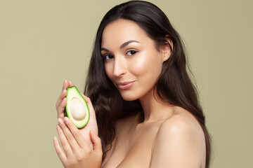 Wall Mural - Young beautiful woman holding avocado half on pistachio background