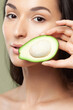 An avocado cut into two pieces in hands of young playful woman