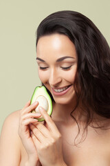 Wall Mural - Young beautiful woman holding avocado half on pistachio background