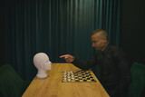 Fototapeta Tęcza - African American man playing checkers at table in team with head mannequin. Concept of business, strategies, competition