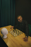 Fototapeta Tęcza - African American man playing checkers at table in team with head mannequin. Concept of business, strategies, competition