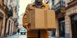 A courier holds a cardboard package in an urban environment.