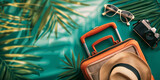 Fototapeta  - A set of essentials for a summer trip: a hat, sunglasses, a camera and a suitcase surrounded by palm leaves on a turquoise background. Summer vacation concept.
