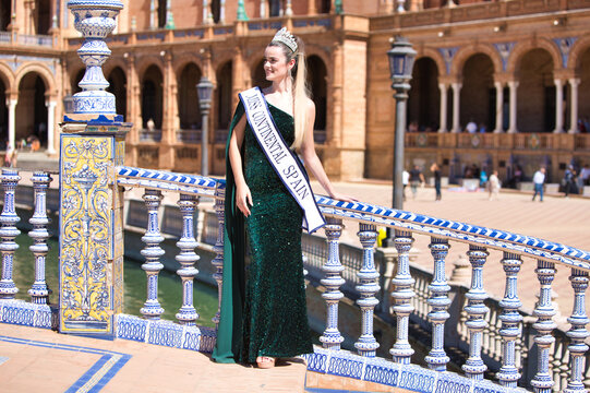 Beautiful young woman winner of a beauty pageant dressed in a green sequined dress and wearing a diamond crown and winner's sash. She is in seville in the famous plaza de espana. 