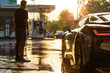 A person stands near a sports car at a gas station washing hic car, illuminated by the golden hues of the setting sun