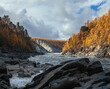 Wild taiga fast river with autumn larch on rocky shores.
