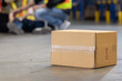 Close up on carton box with background of warehouse staff having an accident