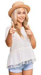 Wall Mural - Young blonde girl wearing summer hat pointing fingers to camera with happy and funny face. good energy and vibes.