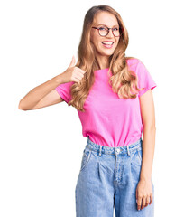 Poster - Young beautiful caucasian woman with blond hair wearing casual clothes and glasses doing happy thumbs up gesture with hand. approving expression looking at the camera showing success.