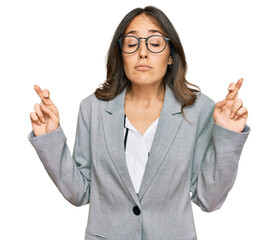 Wall Mural - Young brunette woman wearing business clothes gesturing finger crossed smiling with hope and eyes closed. luck and superstitious concept.