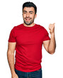 © Krakenimages.com - Hispanic man with beard wearing casual red t shirt smiling with happy face looking and pointing to the side with thumb up.