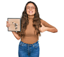 Wall Mural - Young hispanic girl holding drauhgts smiling happy and positive, thumb up doing excellent and approval sign