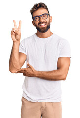 young hispanic man wearing casual clothes and glasses smiling with happy face winking at the camera 