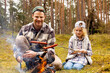 father and daughter spend time together and frying sausages over a bonfire while camping in forest. bonding activities