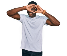 Wall Mural - Young african american man wearing casual white t shirt doing heart shape with hand and fingers smiling looking through sign