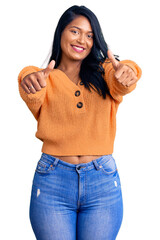 Poster - Hispanic woman with long hair wearing casual winter sweater approving doing positive gesture with hand, thumbs up smiling and happy for success. winner gesture.