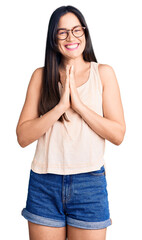 Wall Mural - Young beautiful caucasian woman wearing casual clothes and glasses praying with hands together asking for forgiveness smiling confident.