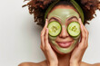 Beautiful woman with cucumber slices on her eyes and face mask on a white background. Rejuvenation and skin care concept.