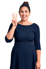 Wall Mural - Young beautiful brunette woman wearing casual dress showing and pointing up with fingers number three while smiling confident and happy.