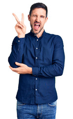 Wall Mural - Young handsome man wearing casual shirt smiling with happy face winking at the camera doing victory sign with fingers. number two.