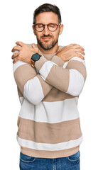 Wall Mural - Handsome man with beard wearing casual clothes and glasses hugging oneself happy and positive, smiling confident. self love and self care