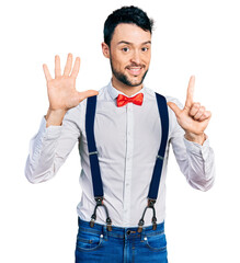 Poster - Hispanic man with beard wearing hipster look with bow tie and suspenders showing and pointing up with fingers number seven while smiling confident and happy.