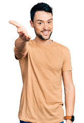 Poster - Hispanic man with beard wearing casual t shirt smiling cheerful offering palm hand giving assistance and acceptance.