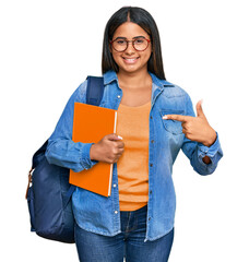 Poster - Young latin girl wearing student backpack and holding books cheerful with a smile on face pointing with hand and finger up to the side with happy and natural expression